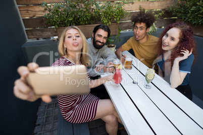 Friends taking selfie with mobile phone while having drinks in bar
