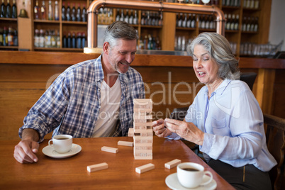 Senior friends playing jenga game on table in bar