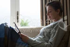 Woman using digital tablet on sofa in living room