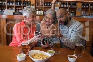 Senior friends using mobile phone in bar