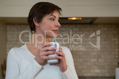 Thoughtful woman having cup of coffee in kitchen