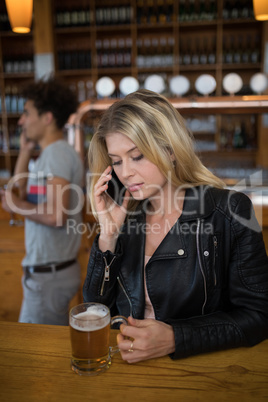 Beautiful woman talking on mobile phone while having glass of beer
