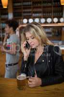 Beautiful woman talking on mobile phone while having glass of beer