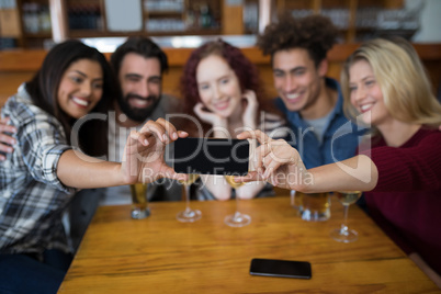 Friends taking selfie with mobile phone while having glass of drinks