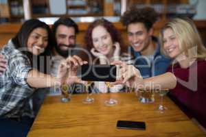 Friends taking selfie with mobile phone while having glass of drinks