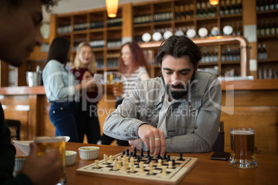 Two men playing chess while having glass of beer