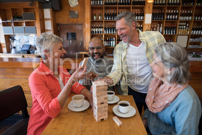 Happy friends playing jenga game while having cup of coffee