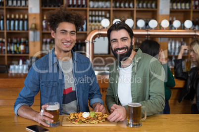 Two male friends having glass of beer and mexican food in bar