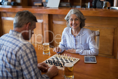 Friends playing chess while having glass of beer in bar