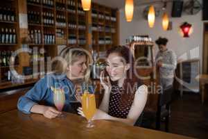 Friends gossiping over the mobile phone while sipping cocktails