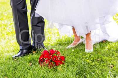 Bridal bouquet is in front of bride and groom in the meadow