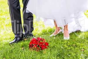 Bridal bouquet is in front of bride and groom in the meadow