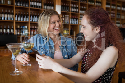 Female friends using mobile phone while having drinks in bar