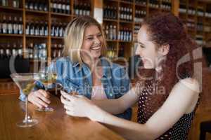 Female friends using mobile phone while having drinks in bar