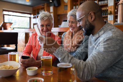 Senior friends using mobile phone in bar