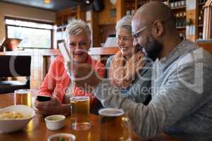 Senior friends using mobile phone in bar