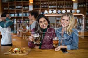 Smiling female friends having glass of beer in bar