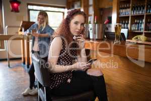 Beautiful woman sitting on chair and using mobile phone at counter