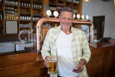Smiling senior man using mobile phone while having glass of beer