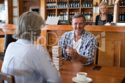 Senior friends playing jenga game on table in bar