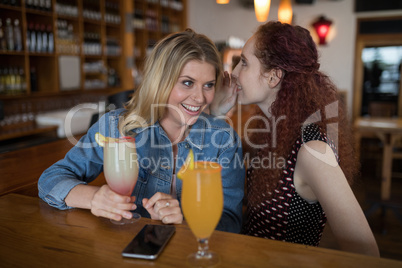 Woman whispering in her friends ears at counter