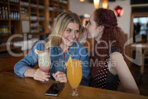 Woman whispering in her friends ears at counter