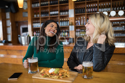 Two female friends having glass of beer and mexican food in bar