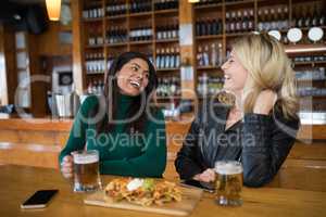 Two female friends having glass of beer and mexican food in bar