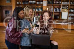 Female friends using mobile phone while having drinks in bar