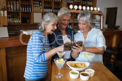 Senior female friends using digital tablet while having drinks