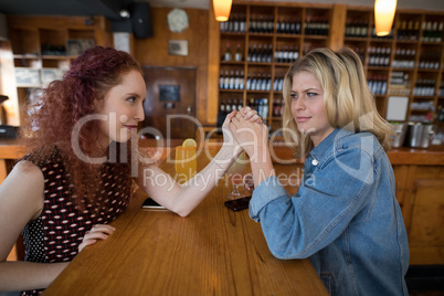 Female friends arm wrestling in bar