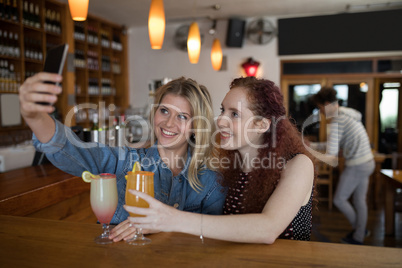 Female friends taking selfie with mobile phone while having drinks in bar