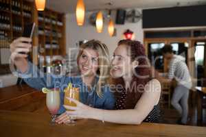 Female friends taking selfie with mobile phone while having drinks in bar
