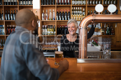 Man talking to senior waitress while having glass of beer at counter