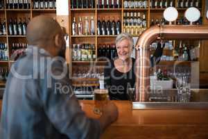 Man talking to senior waitress while having glass of beer at counter