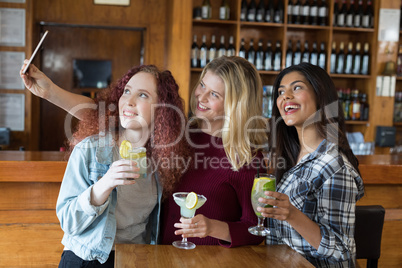 Female friends taking selfie with mobile phone while having drinks in bar