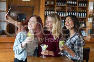 Female friends taking selfie with mobile phone while having drinks in bar