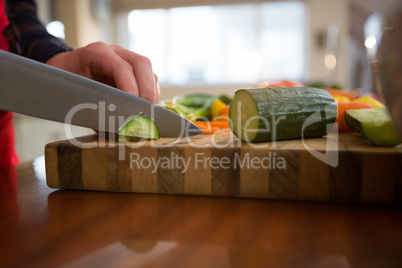 Mid section of woman cutting vegetable in kitchen