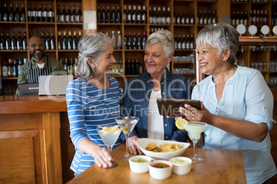 Senior female friends using digital tablet while having drinks