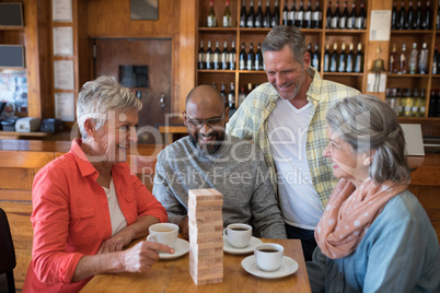 Happy friends playing jenga game while having cup of coffee