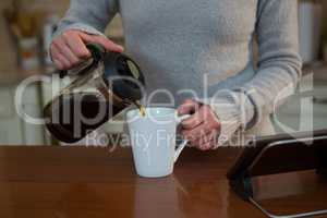 Woman pouring coffee into mug in kitchen