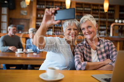 Senior friends taking selfie with mobile phone in restaurant