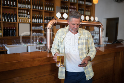 Senior man using mobile phone while having glass of beer