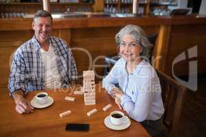Senior friends playing jenga game on table in bar