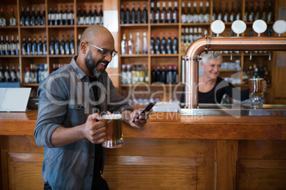 Man using mobile phone while having glass of beer in bar