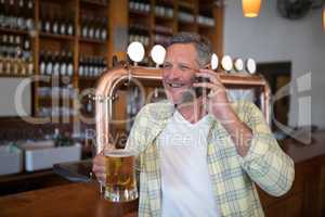 Smiling senior man talking on mobile phone while having glass of beer