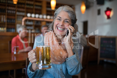 Smiling senior woman talking on mobile phone while having glass of beer