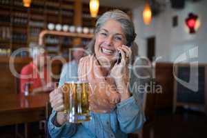 Smiling senior woman talking on mobile phone while having glass of beer