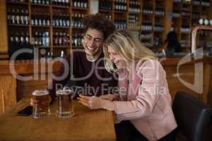 Couple using mobile phone while having glass of beer in bar