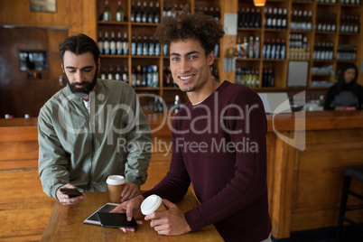 Two male friends using mobile phone while having coffee